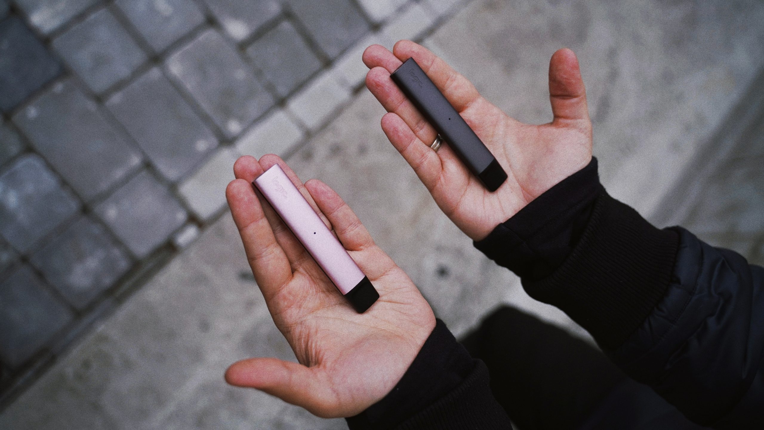Two hands holding vape pens, one pink, one grey.