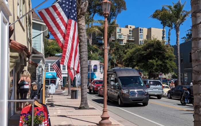 Capitola Village on a sunny day with an American flag hanging from a business and blue skys.