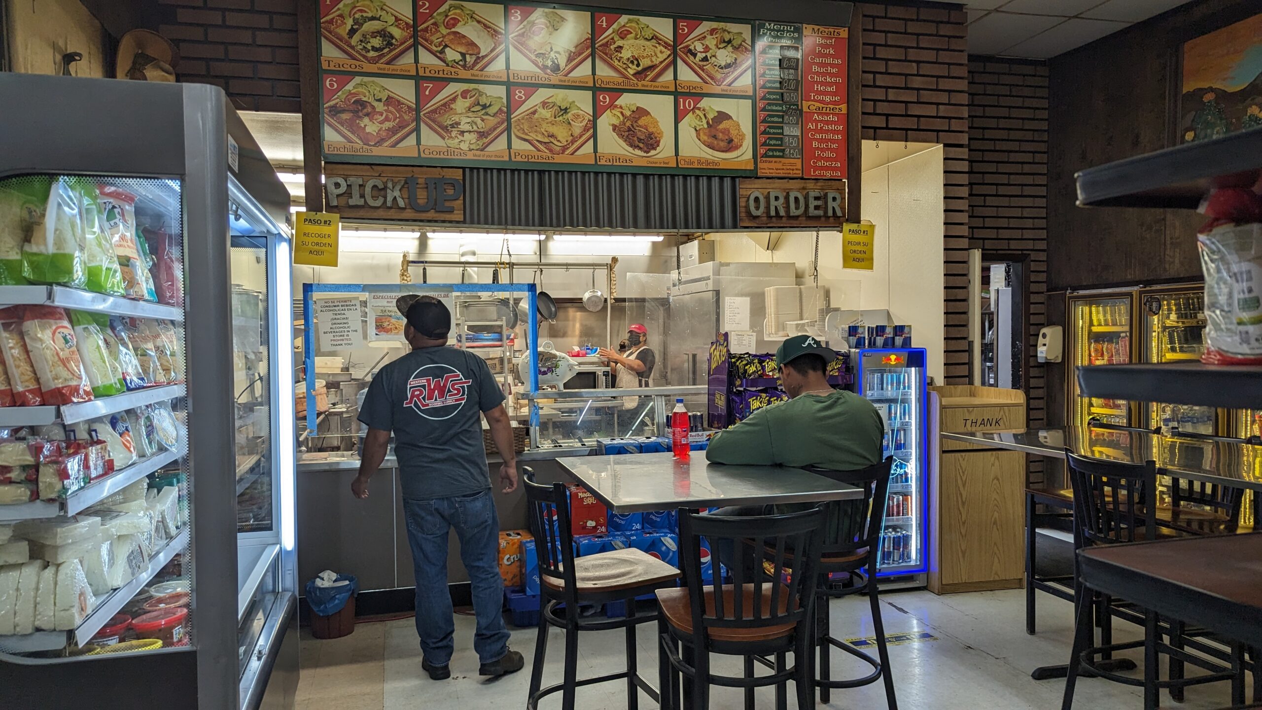 A man stands at the counter of the deli inside Pajaro Food Center, and another man sits at a table.