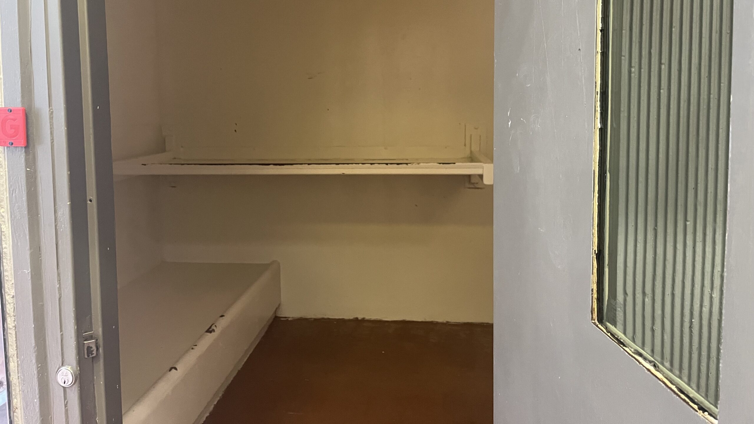 A door stand ajar to a cell in the Santa Cruz Main Jail. There is a built in bench and shelf.