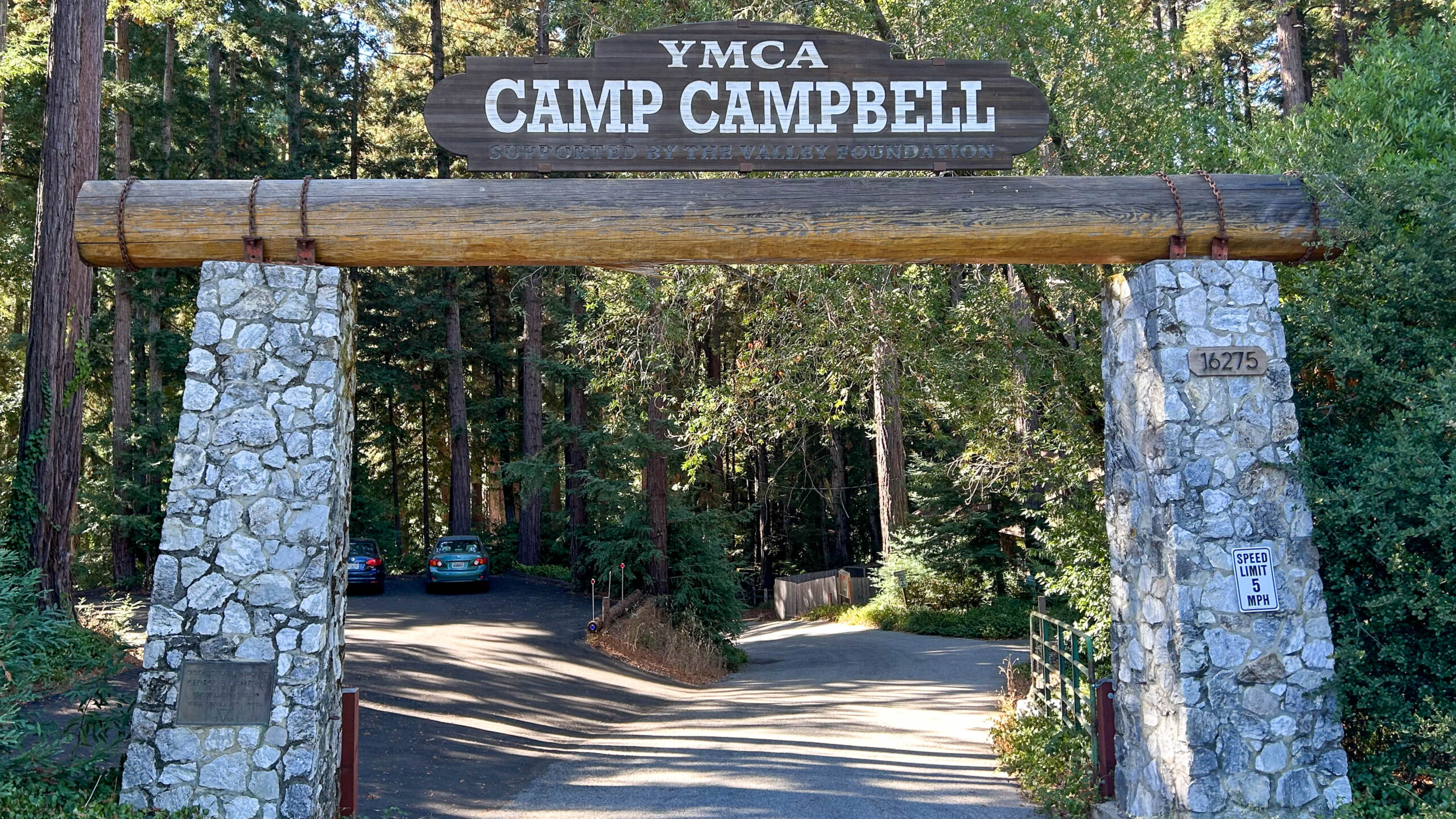 La entrada al Campamento YMCA Campbell en Boulder Creek es un arco de piedra y madera. Un camino serpentea hacia el bosque de secuoyas.