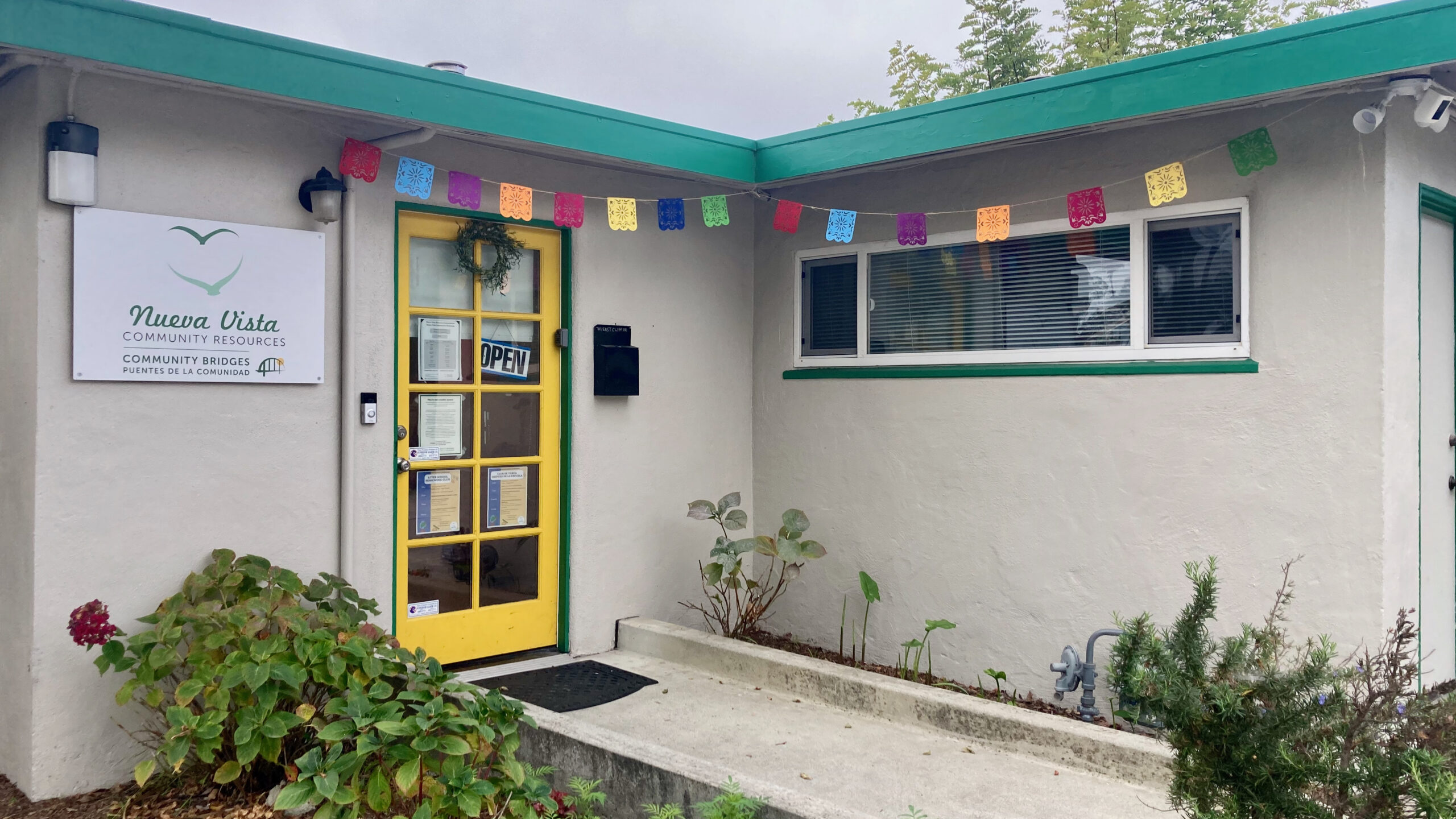 Nueva Vista Community Resources in Santa Cruz has a yellow door and papel picado decorating the entrance.