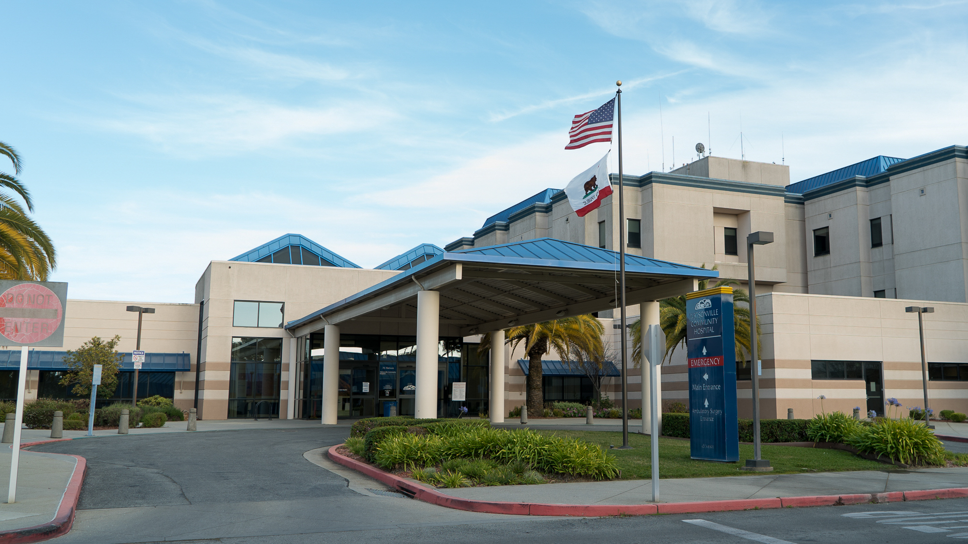 The Watsonville Community Hospital with a blue sky and a flag pole in front with the U.S. and California state flags.