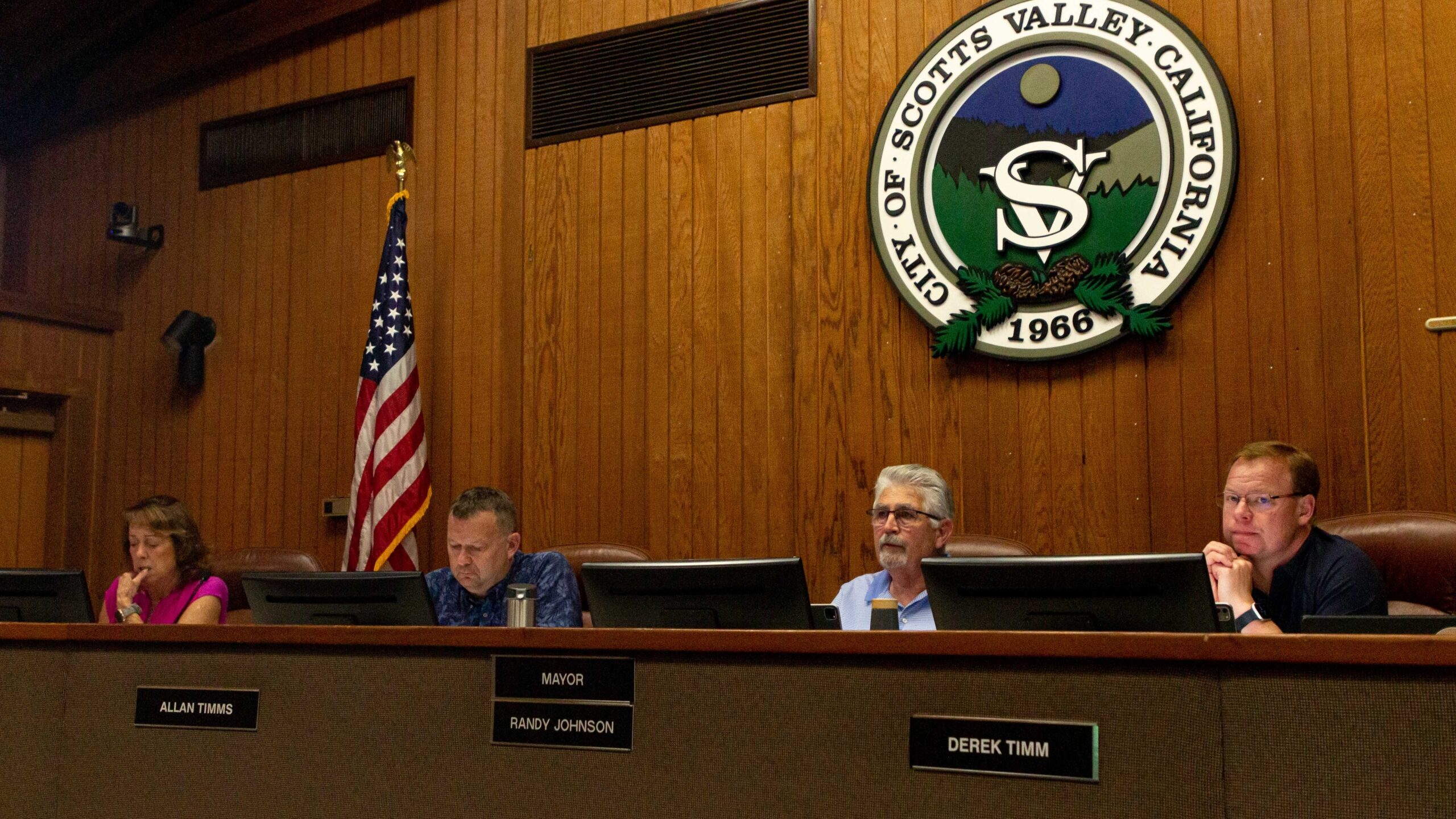 A photo of four Scotts Valley city council members sitting at the dais. Behind them are a city emblem on the wall and an American flag.