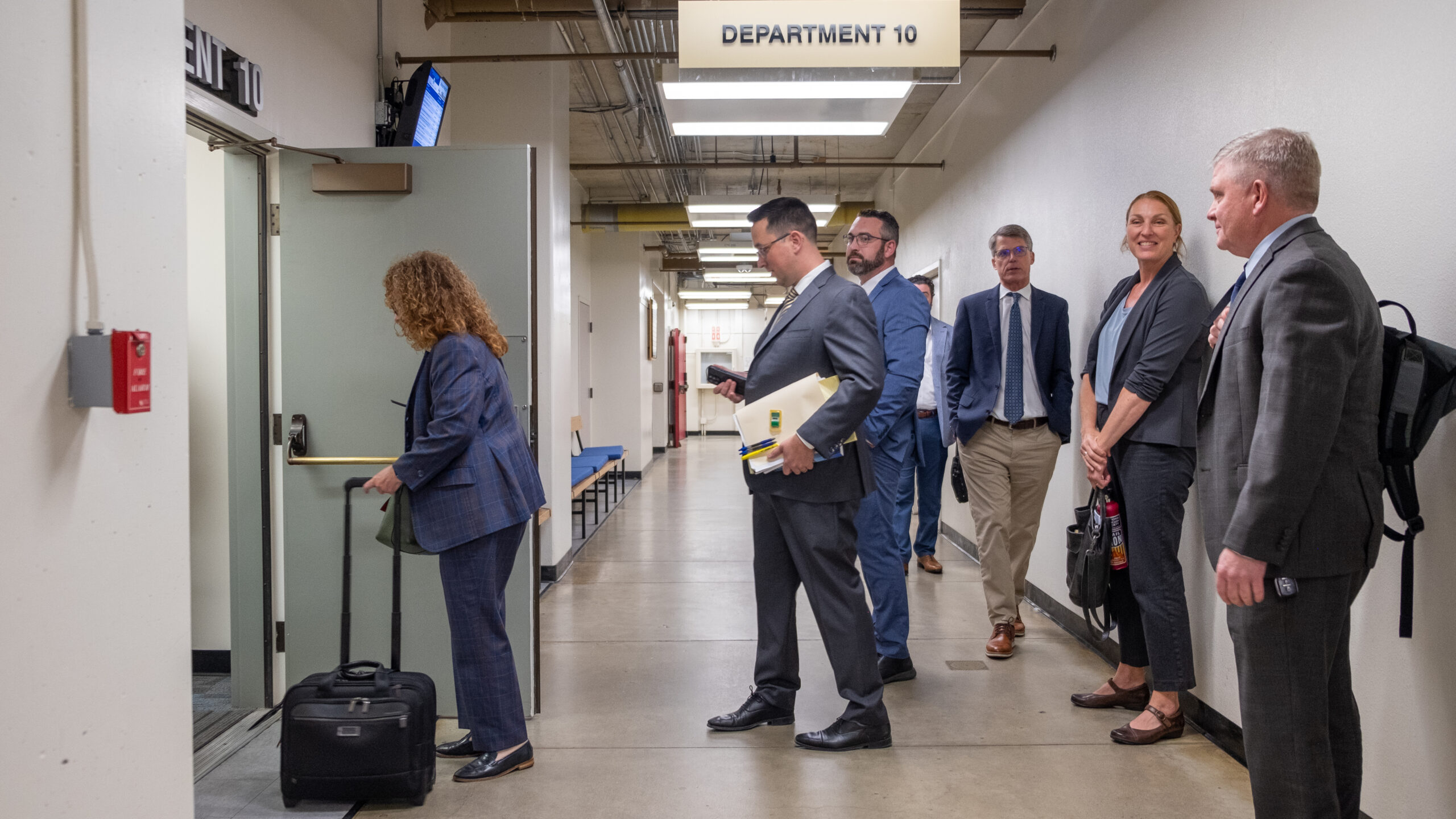 A photo of seven attorneys standing in an otherwise empty hallway waiting to enter a courtroom in the county building on Ocean Street. A sign hangs above them reading "Department 10."