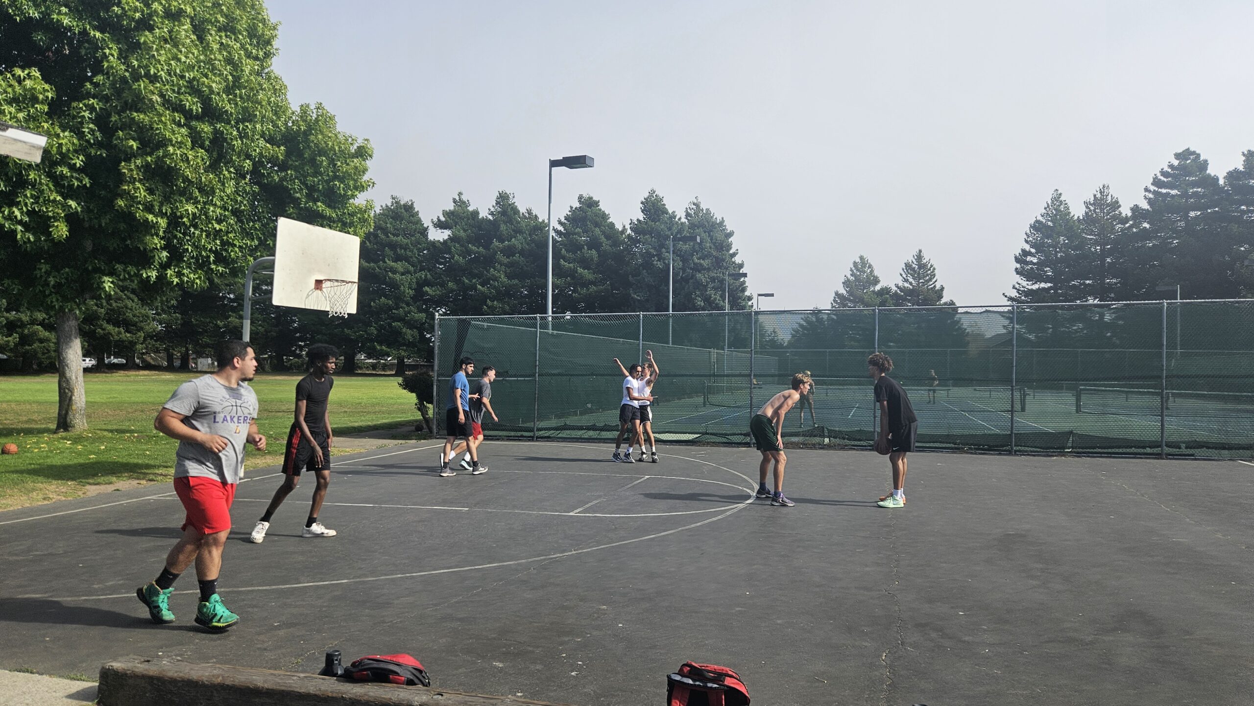 Half a dozen people are on a basketball court playing a game, one person holds the ball and looks to be preparing to shoot.