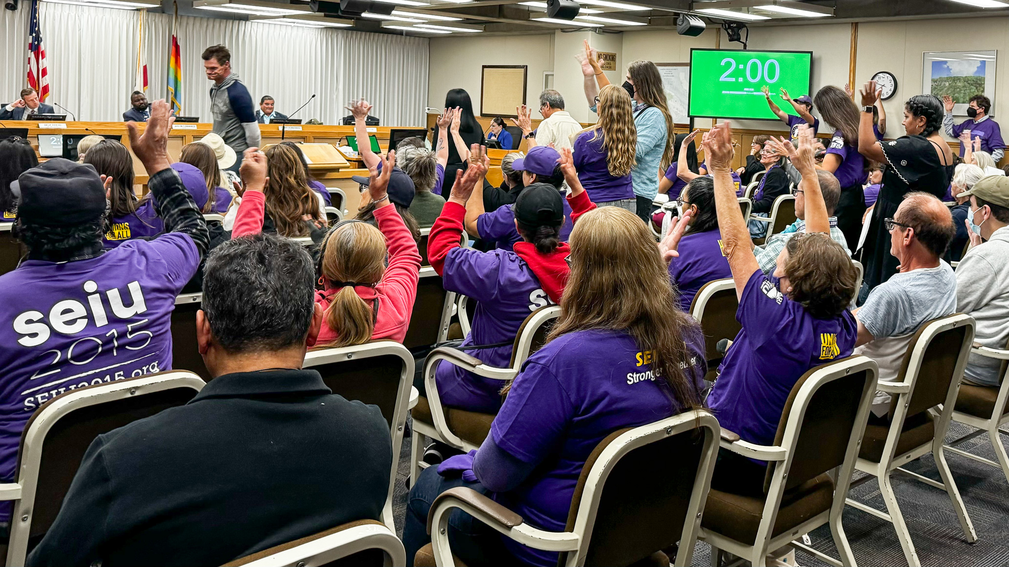 board-of-supervisors-ihss-aug-13-2024-1 Workers represented by SEIU Local 2015 and other unions wave their hands in support of speakers at a Santa Cruz County supervisors meeting Aug. 13. Caregivers employed through the county’s In-Home Supportive Services program have demanded higher pay. (Jesse Kathan — Santa Cruz Local)