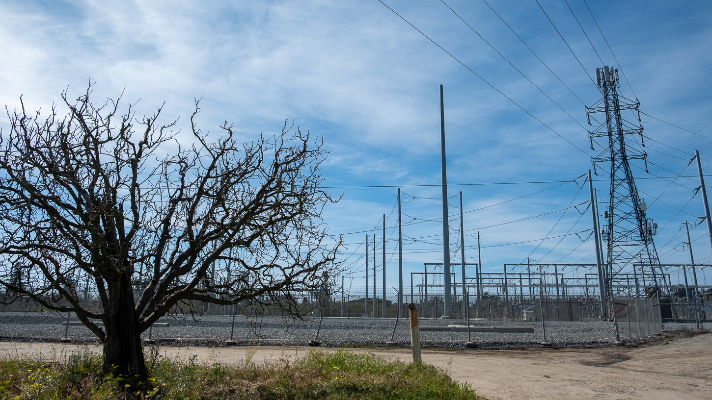 90-minto-road-bess-lithium-battery-altenberg-3-25-2025-1 A PG&E substation and its transmission towers are seen behind an apple tree. An apple orchard across from the substation is the site of a proposed lithium battery facility.