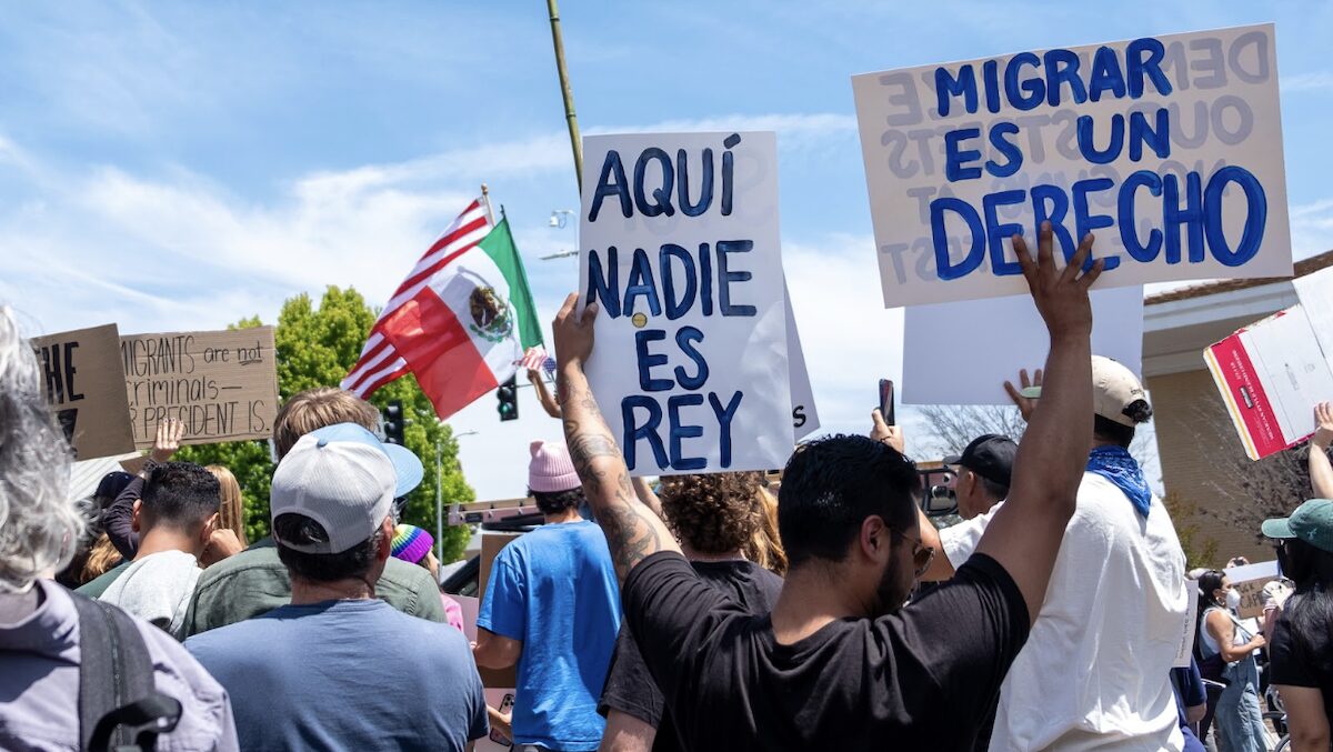 Protesters gather in Santa Cruz on June 14 to oppose President Donald Trump and his policies. A protester holds signs that say in Spanish ‘Here no one is king’ and ‘Migration is a right.’ (Nik Altenberg — Santa Cruz Local file)